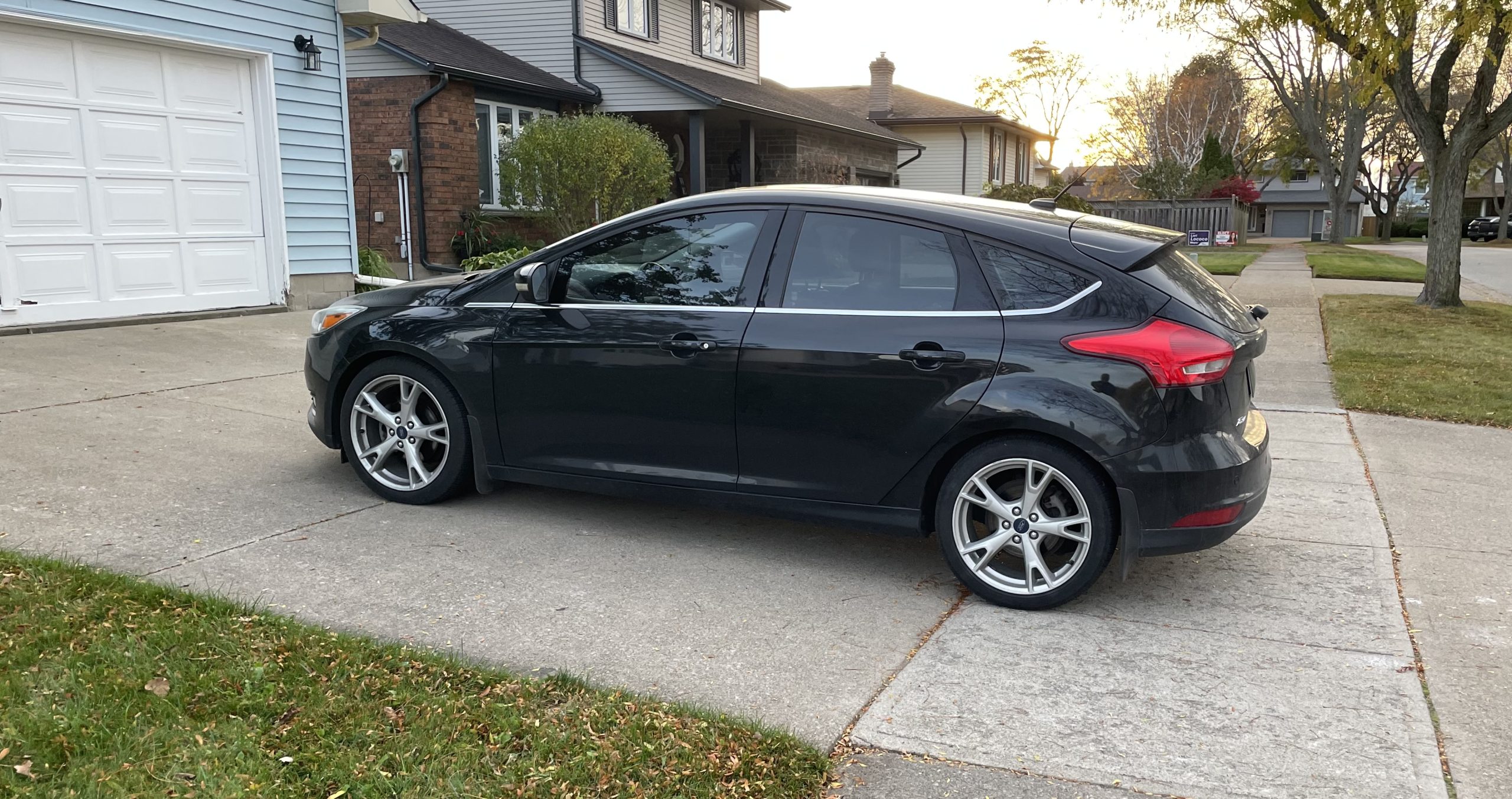 A car parked in a driveway blocking more than half of the sidewalk. There is however, plenty of room for the car to move forward and not block anything or anybody.